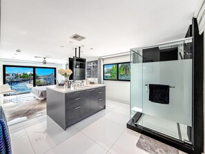A modern bathroom with a glass shower enclosure, a large mirror, and a view of a pool and cityscape.