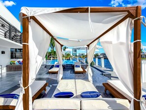 Ein Strandloungebereich mit Baldachin, mehreren Liegestühlen und Blick auf Pool und Meer.