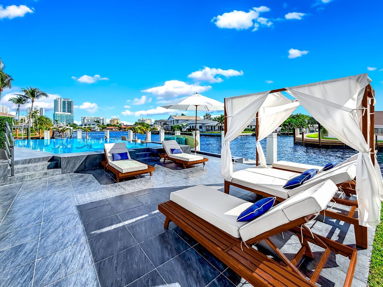 A poolside area with lounge chairs and umbrellas, a clear blue sky, and a view of buildings in the background.