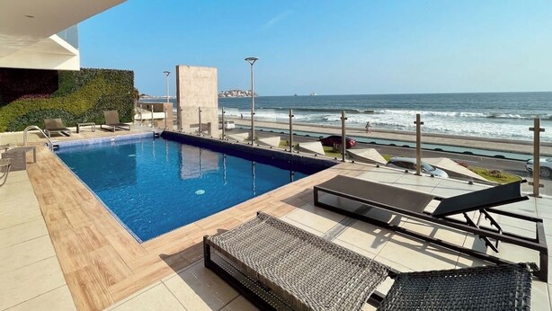 An infinity pool with a view of the ocean, lounge chairs, and a clear sky. - Contemporary Condo with Ocean Views (Mazatlan)