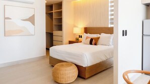 Ein modernes Hotelzimmer mit einem großen Bett, einem Kleiderschrank, einem Nachttisch mit Lampe und einem Weidenhocker.