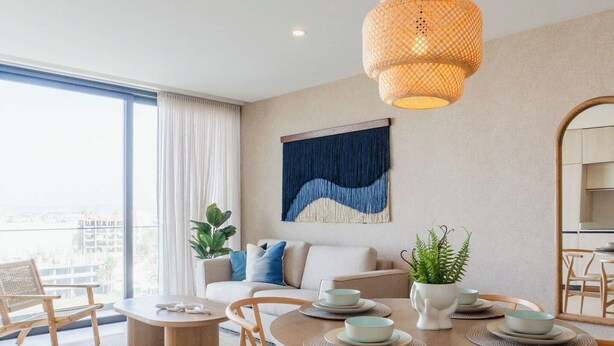 Ein modernes Wohnzimmer mit Essbereich, großen Fenstern, einer Pendelleuchte und einem blauen abstrakten Gemälde.