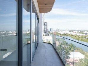 A balcony with a glass railing, a view of a river, and a cityscape in the background. - Luxury apt on the Malecón with lagoon views (Mazatlan)