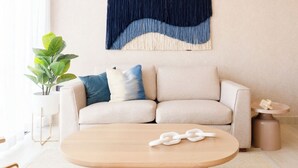 Ein Wohnzimmer mit beiger Couch, einem Holztisch, einem Blumentopf und einer Wanddekoration.
