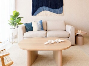 Ein Wohnzimmer mit beiger Couch, einem Holztisch, einem Blumentopf und einer Wanddekoration.