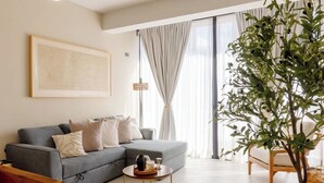 Una sala de estar con un sofá gris, una mesita redonda, una planta y una silla de mimbre.