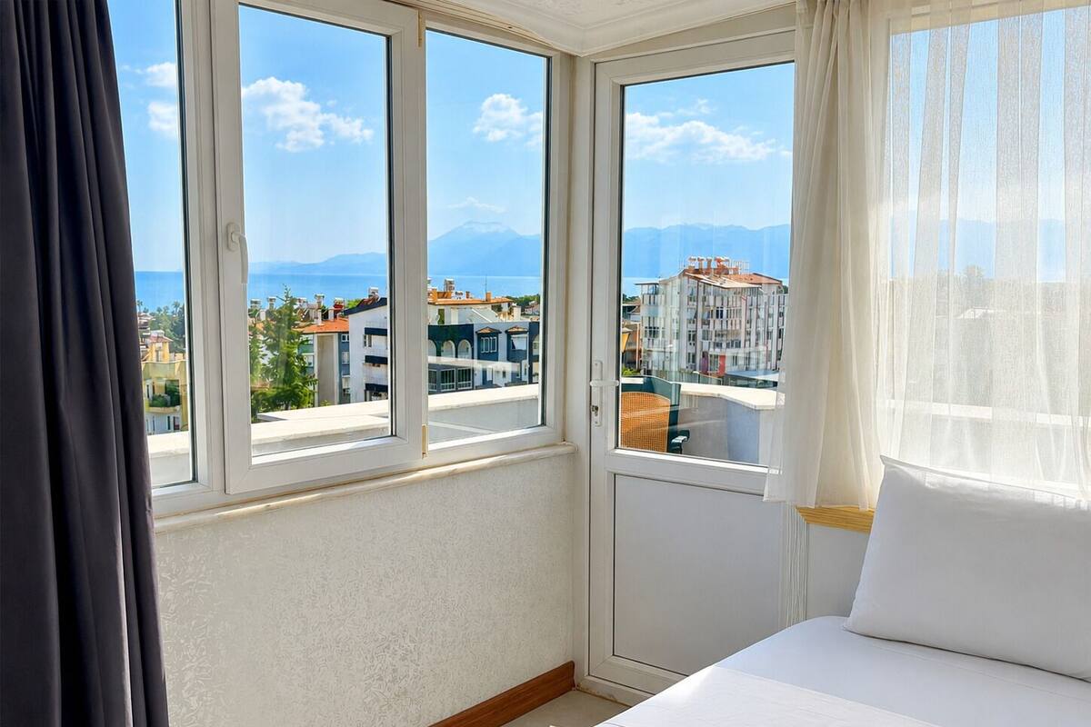 A hotel room with a large window, a bed, and a view of buildings and mountains.