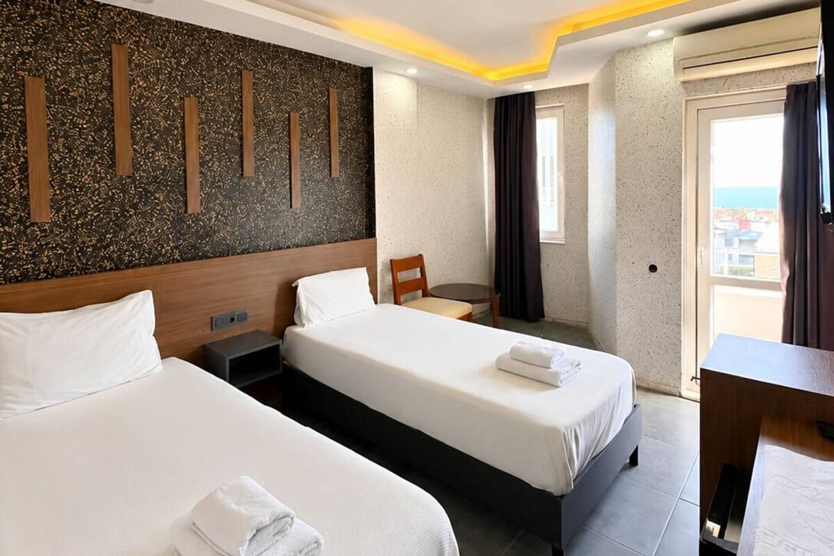 A hotel room with two beds, a desk, a chair, and a view of the city.