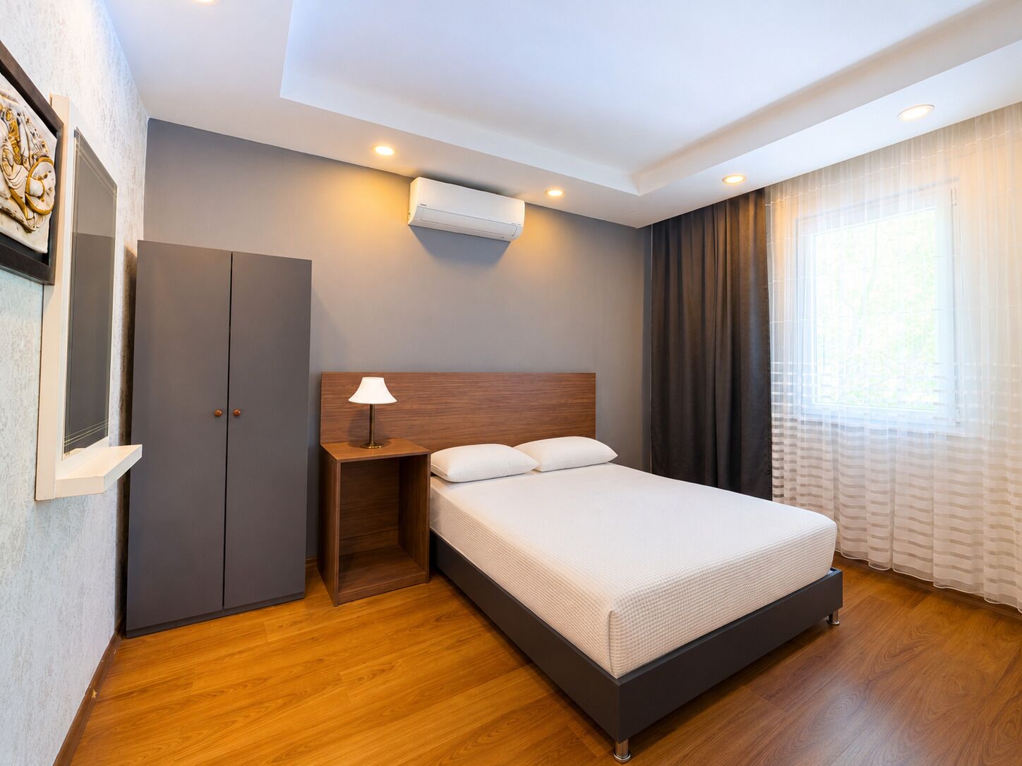Une chambre d’hôtel moderne équipée d’un lit, d’une lampe de chevet, d’une armoire, d’un climatiseur et d’une fenêtre avec des rideaux.