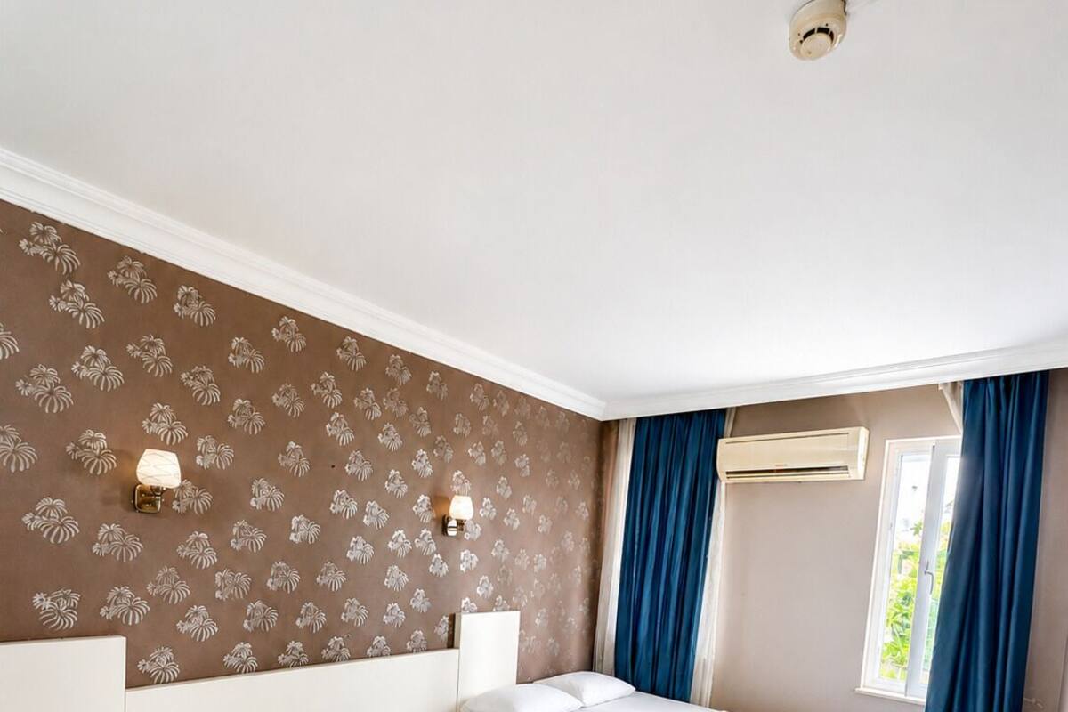 A hotel room with two beds, a wall-mounted air conditioner, and a window with curtains.