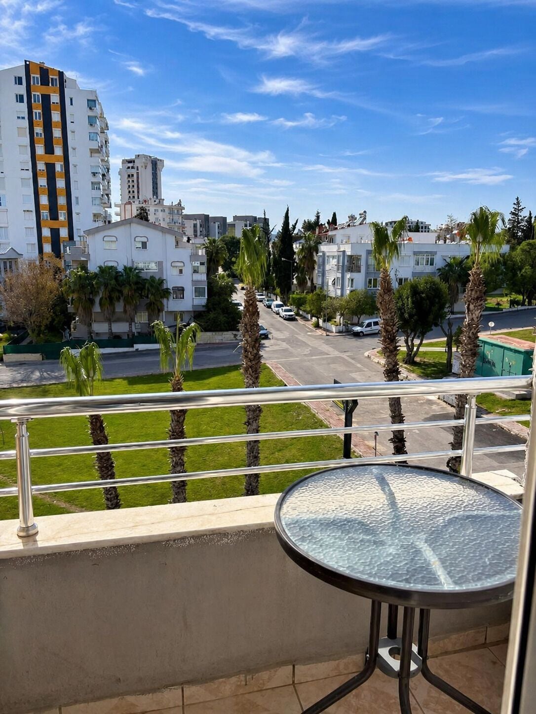 A balcony with a view of a residential street, palm trees, and modern buildings.