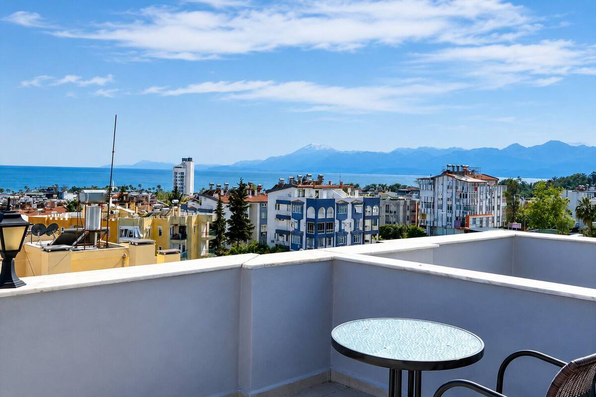 A balcony with a table and chairs, overlooking a cityscape with buildings and a distant mountain range.