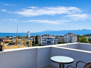 A balcony with a table and chairs, overlooking a cityscape with buildings and a distant mountain range. - Luna Hotel (Güzeloba)
