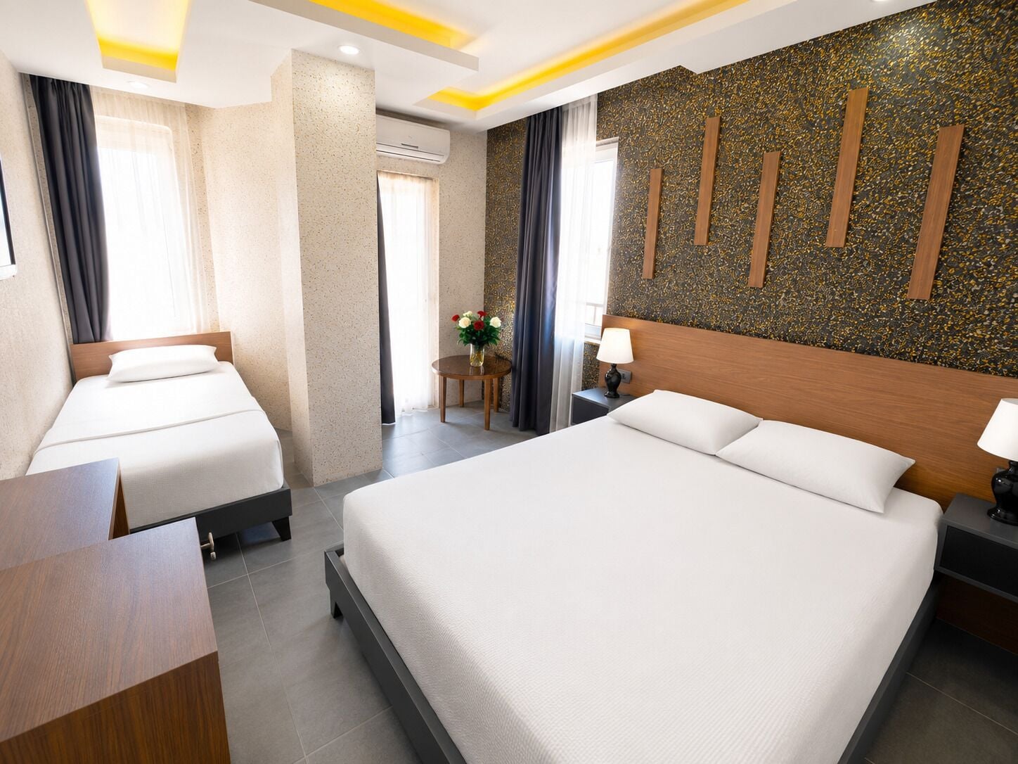 A hotel room with two beds, a small table with a vase of flowers, a lamp, and a decorative wall.
