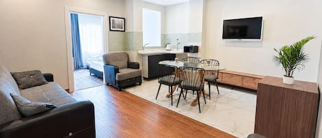Una sala de estar moderna con un sofá, un comedor con sillas, una cocina con un fregadero y un televisor montado en la pared.