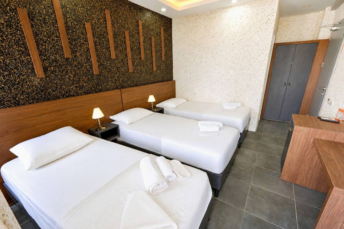 A hotel room with three beds, a wooden headboard, a minibar, and a desk.