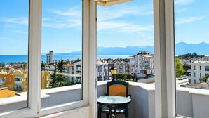 Un balcón con una mesa y una silla, con vistas a una ciudad costera con edificios y montañas.