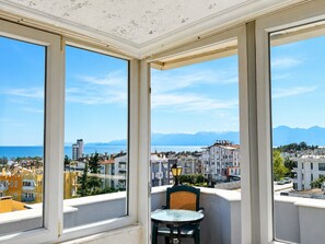 A balcony with a table and chair, overlooking a coastal cityscape with buildings and mountains. - Luna Hotel (Güzeloba)