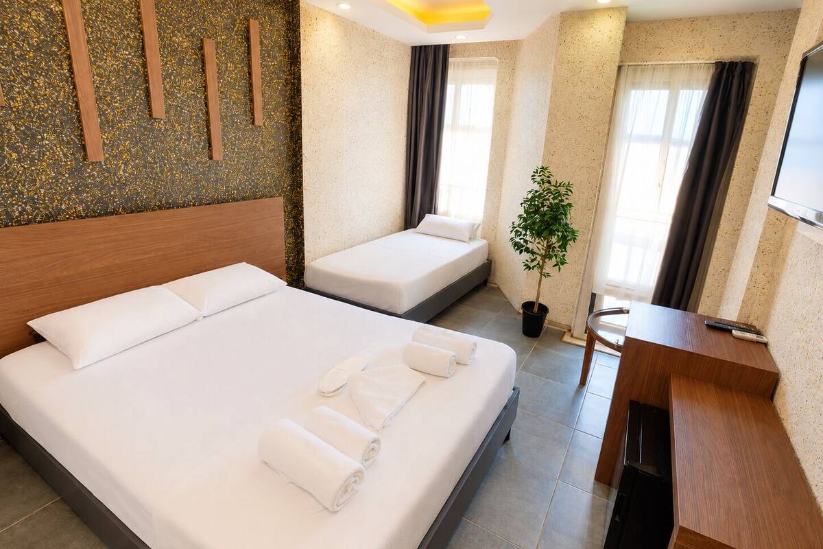 A hotel room with a large bed, a smaller bed, a desk, a potted plant, and a TV.