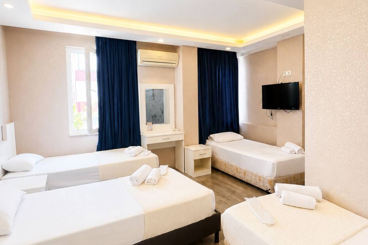 A hotel room with three beds, a TV, an air conditioning unit, and a window with curtains.