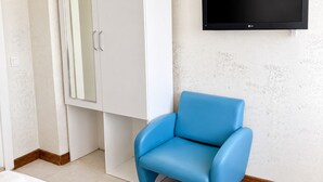 Una habitación con un armario blanco, una silla azul y un televisor montado en la pared.