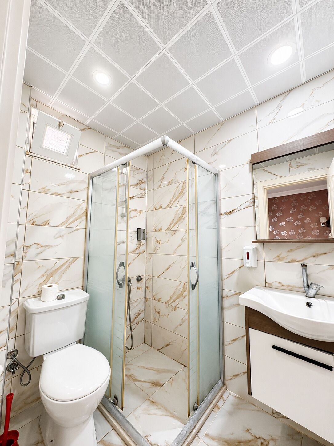 Un bany amb plat de dutxa tancat amb vidre, un vàter i un lavabo amb mirall a la part superior.