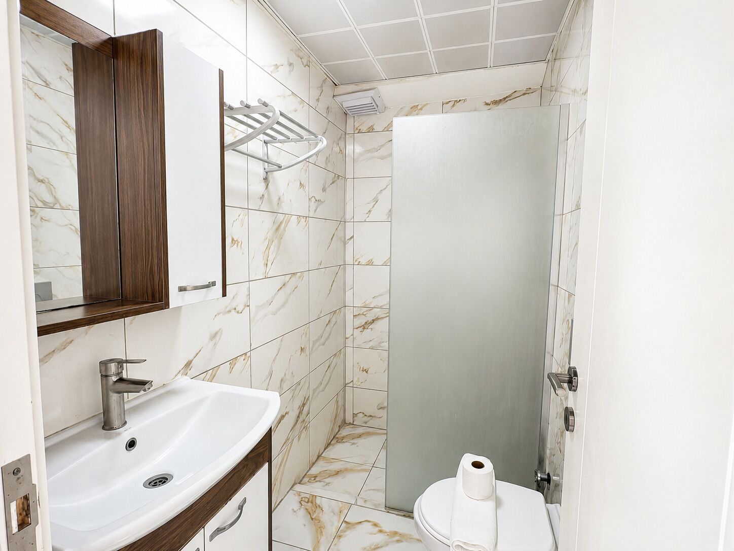 Een badkamer met een wastafel, spiegel, handdoekhouder, toilet en douchedeur.