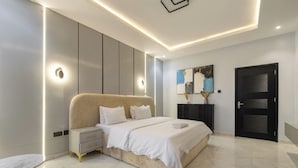 Un dormitorio moderno con cama, mesitas de noche, un sillón rojo, una puerta negra y obras de arte en la pared.