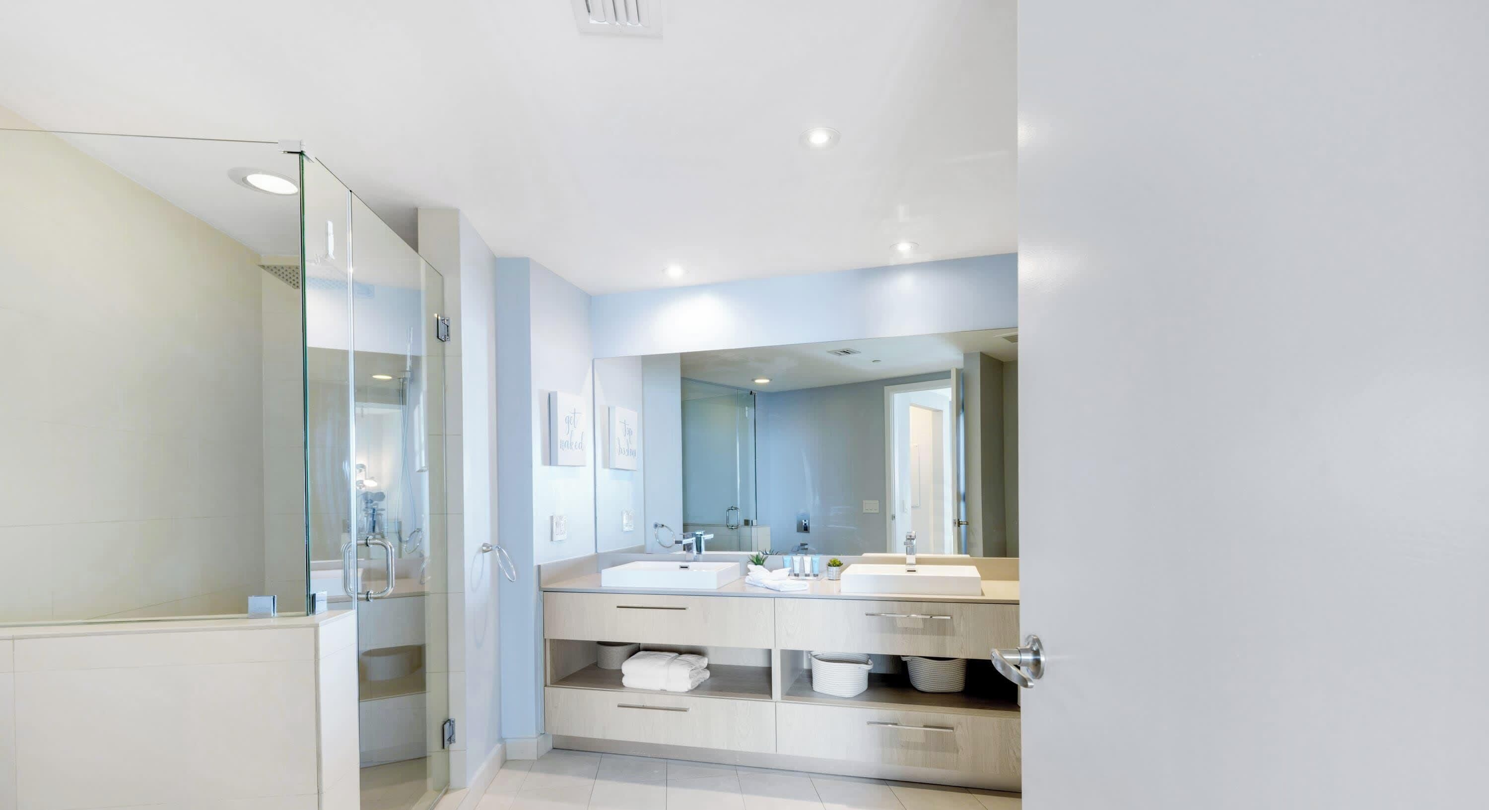 A modern bathroom with a glass shower enclosure, two sinks, and a large mirror.