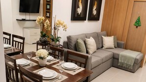 A dining area with a wooden table set for four, a grey sofa, and a small Christmas tree decoration. - Luxe 1-bedroom Condo Front of Mall of Asia With City View in Pasay (Pasay)