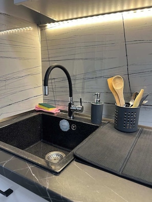 A kitchen with a black sink, stainless steel faucet, and a utensil holder with wooden spoons. - Budget Cute Studio in Thessaloniki Center (Thessaloniki)