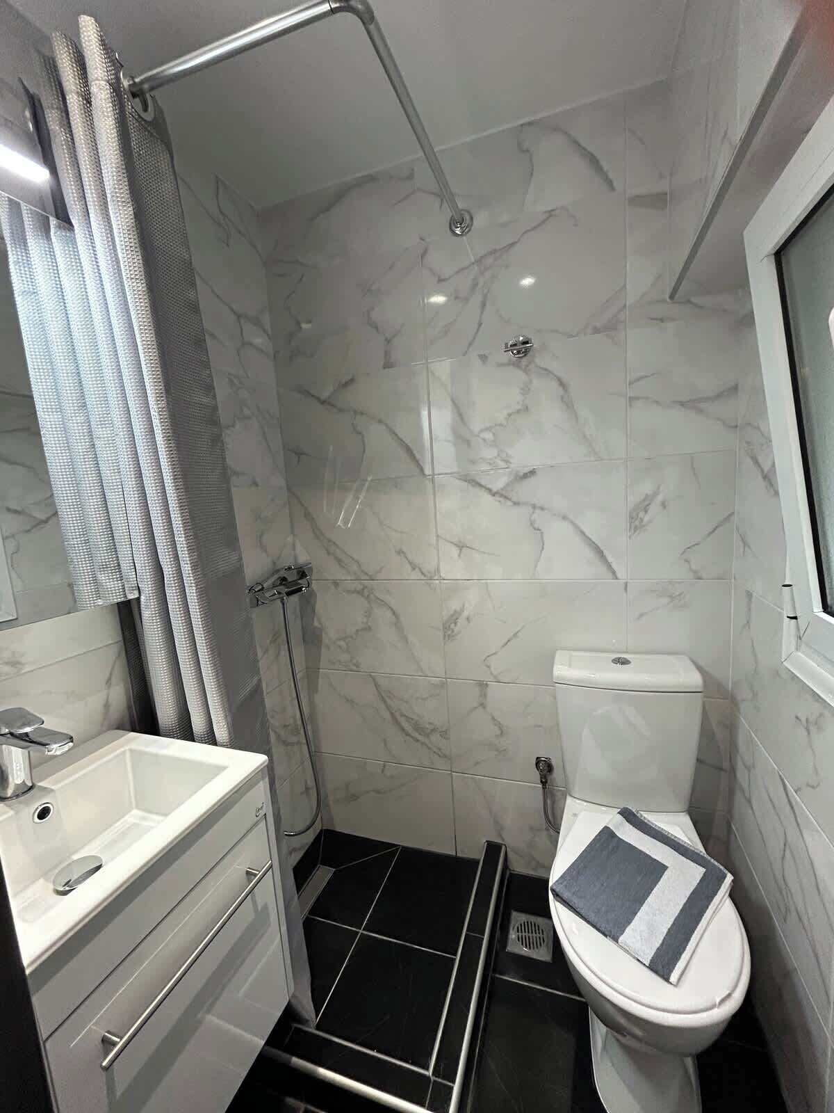 Een badkamer met douche, toilet, wastafel en spiegel.