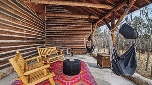 Une cabane en rondins avec un banc en bois, un hamac et un tapis aux couleurs vives.