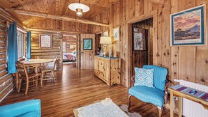L’intérieur d’une cabane en rondins comprend un coin repas, un canapé, une lampe et un tableau encadré accroché au mur.