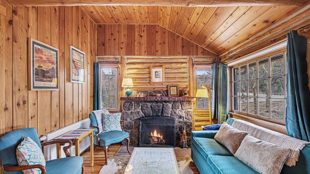 L’intérieur d’une cabane en rondins, avec une cheminée en pierre, des murs en bois, un canapé bleu et une table servant de carte.