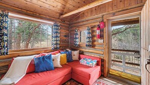 L’intérieur d’une cabane en rondins, avec un canapé d’angle rouge, des rideaux à motifs et un extincteur.