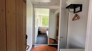 A hallway with a wooden door, a round orange rug, a small table with a chair, and a hanging coat rack.