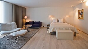 A modern hotel room with a bed, a sofa, a small table, and a lamp.