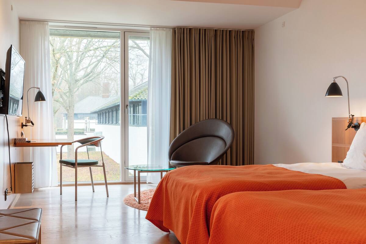 A hotel room with a bed, a desk, a chair, and a window with curtains.
