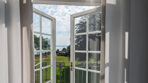 A view through a glass door with a metal railing, leading to a balcony with a grassy area and trees.
