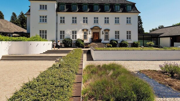 A large, white building with a symmetrical facade, multiple windows, and a central entrance with a door.
