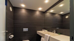 A modern bathroom with dark tiles, a toilet, a sink with a mirror, and a towel rack.