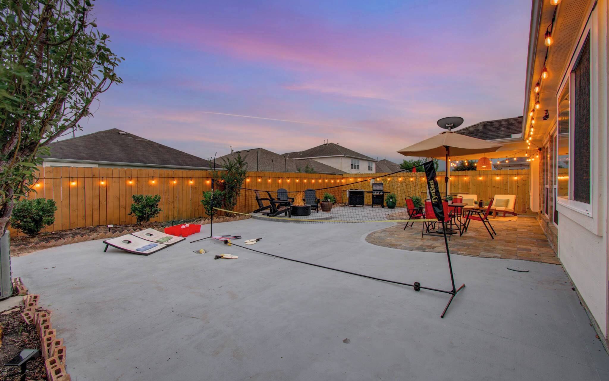 A backyard with a barbecue area, outdoor seating, and string lights.