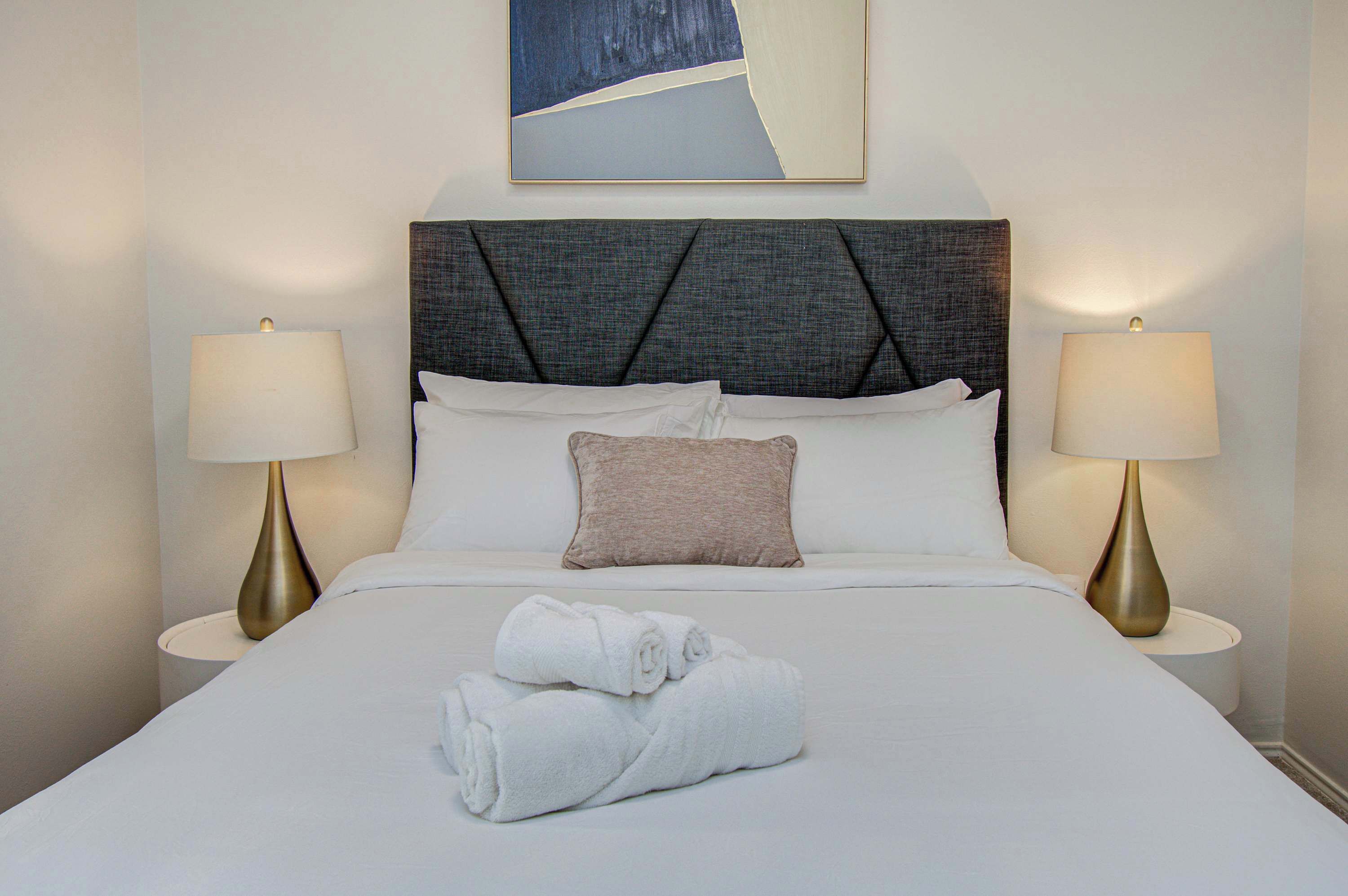 A neatly made bed with white linens, two bedside lamps, and a single pillow.