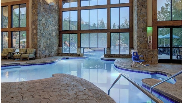 Ein großes Hallenbad mit Steinwänden, großen Fenstern und einem Deckenventilator.
