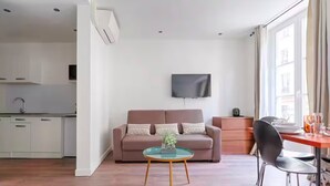 A modern living room with a sofa, a coffee table, and a TV. There is a kitchen area with cabinets and a sink. - UrbanFlat 203 + 202 - 249 Saint Denis SD1 (Paris)