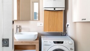 A compact bathroom with a sink, mirror, and a washing machine.