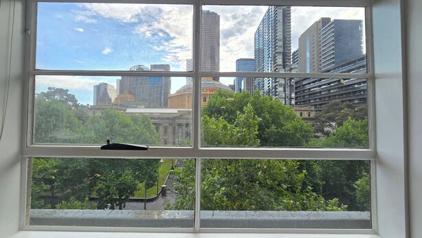 Ein Fenster mit Blick auf eine Stadtlandschaft, darunter hohe Gebäude und Grünflächen.