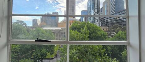 A window with a view of a cityscape, including tall buildings and greenery.