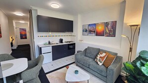 Ein kompakter Wohnbereich mit Küchenzeile, einem grauen Sofa, einem kleinen Esstisch und einem Couchtisch.